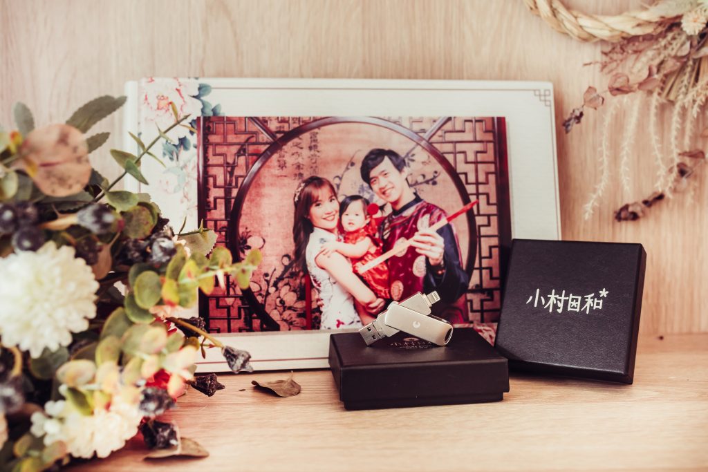 木質背景所拍攝的兒童攝影的周邊商品，包含隨身碟極大本兒童相本，旁邊有乾燥乎作為裝飾