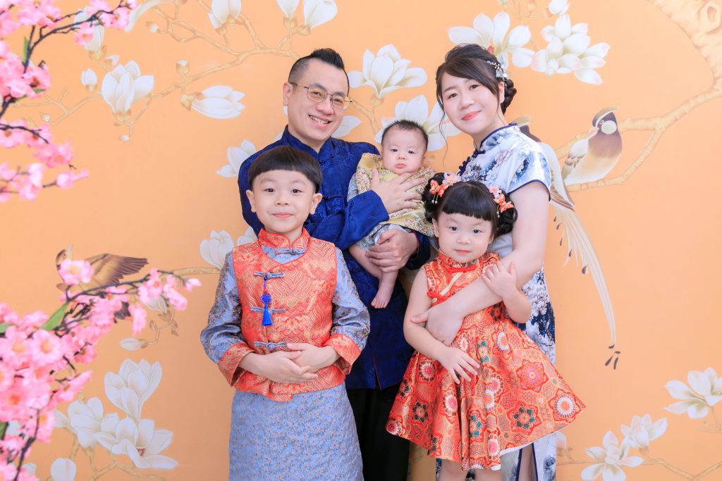 一家五口穿著華麗中式服飾，搭配花鳥背景，呈現經典復古風格的全家福攝影。
