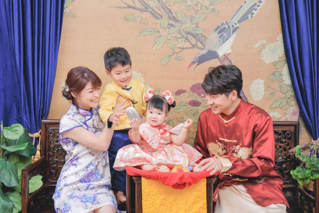 全家一起參與寶寶抓周儀式，寶寶坐在抓周椅上拿取道具，爸爸媽媽與哥哥穿著傳統服裝，溫馨記錄一歲成長時刻
