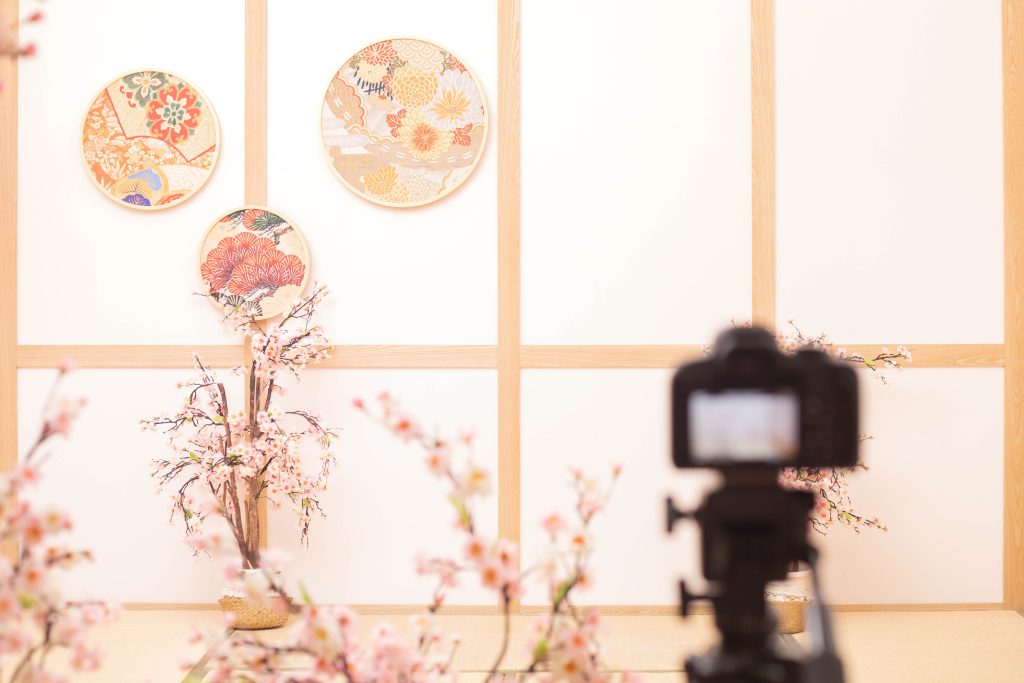 日式抓周攝影場景佈置，榻榻米空間搭配和風圓盤與櫻花裝飾，攝影機架設中，記錄抓周拍攝的準備畫面