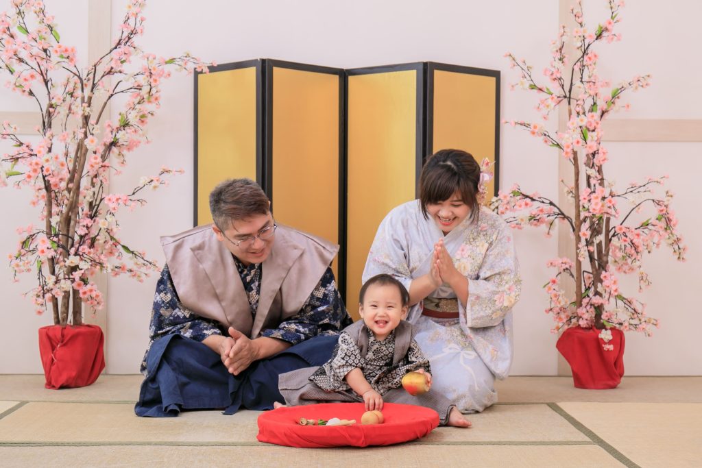 寶寶抓周儀式全家福，爸爸媽媽陪伴寶寶坐在榻榻米上抓周，道具擺放於紅墊上，溫馨記錄一歲重要儀式